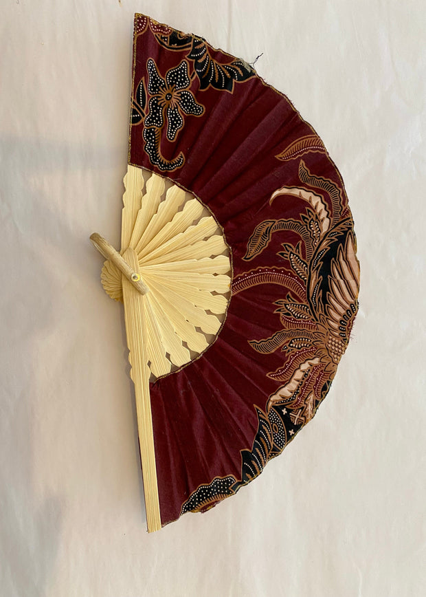 Decorative wall fan with maroon and gold design on a beige background