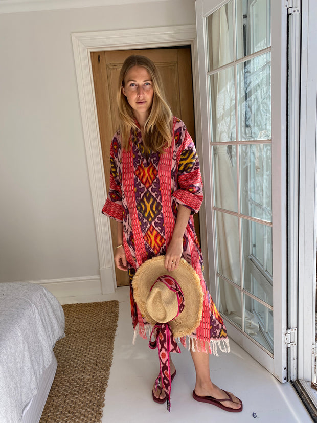 Woman in a colorful dress holding a hat indoors. Oversized Beach Shirt Dress - Watermelon Pink Ikat iridescent sea Fremantle, Perth