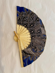 Handheld fan with black and blue patterned cover and beige wooden handle on a white background