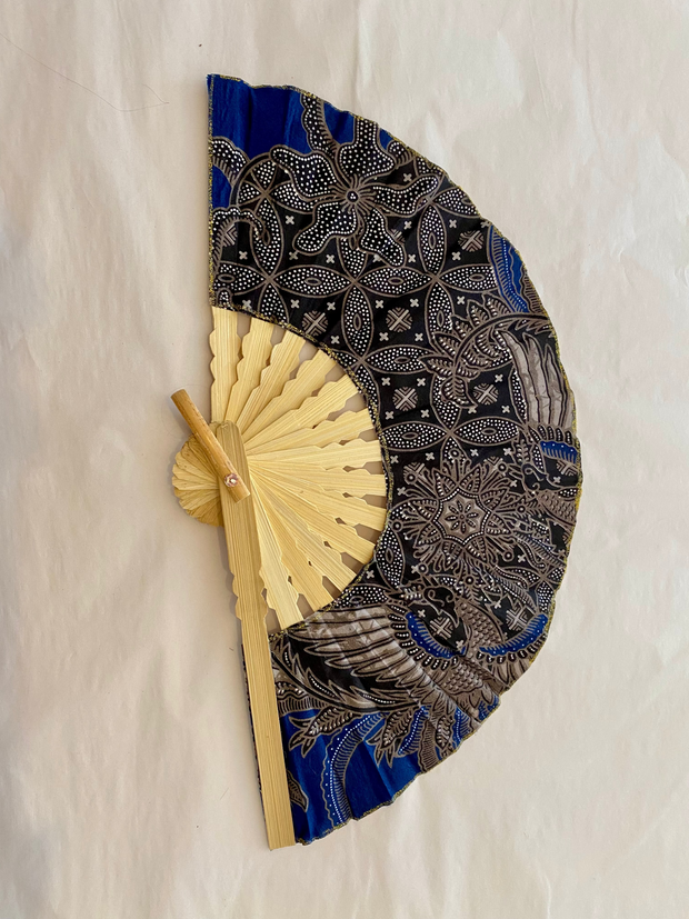 Handheld fan with black and blue patterned cover and beige wooden handle on a white background