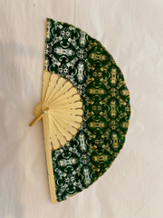Handheld fan with green batik patterned cover and bamboo handle on a light background