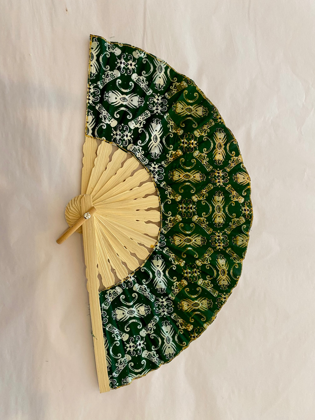 Handheld fan with green batik patterned cover and bamboo handle on a light background