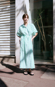 Woman wearing a green and white striped dress standing in front of a building entrance. AMERICAN VINTAGE Zatybay Dress in Neon Lagoon Stripes Iridescent sea Fremantle Perth