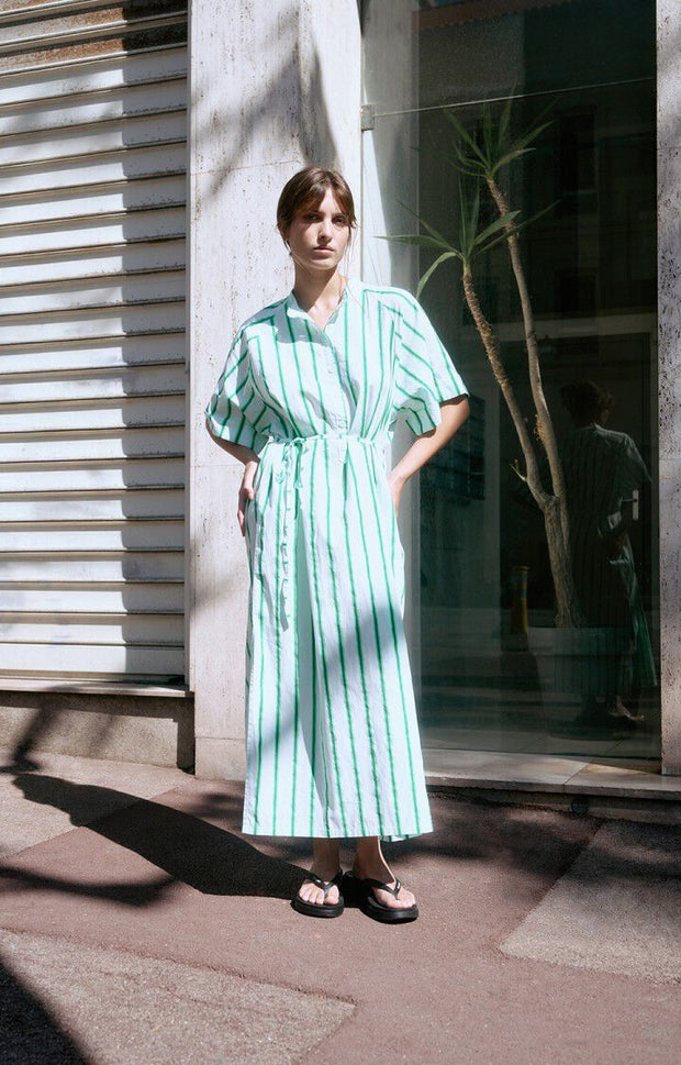 Woman wearing a green and white striped dress standing in front of a building entrance. AMERICAN VINTAGE Zatybay Dress in Neon Lagoon Stripes Iridescent sea Fremantle Perth