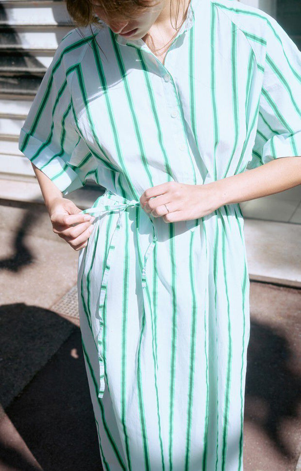 Woman wearing a green and white striped dress standing in front of a building entrance. AMERICAN VINTAGE Zatybay Dress in Neon Lagoon Stripes Iridescent sea Fremantle Perth