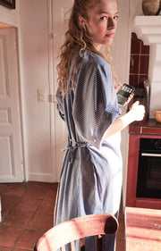 Woman in a blue striped dress standing in a kitchen with a red oven. AMERICAN VINTAGE Zatybay Dress in Aqua Stripes Iridescent Sea Fremantle Perth