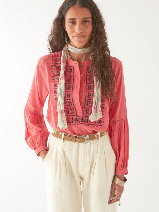Woman wearing a pink embroidered blouse with a white scarf and beige pants on a white background MAISON HOTEL Shanti Blouse in Strawberry fields Iridescent Sea Fremantle