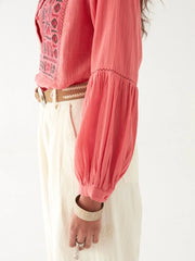Woman wearing a pink embroidered blouse with a white scarf and beige pants on a white background MAISON HOTEL Shanti Blouse in Strawberry fields Iridescent Sea Fremantle