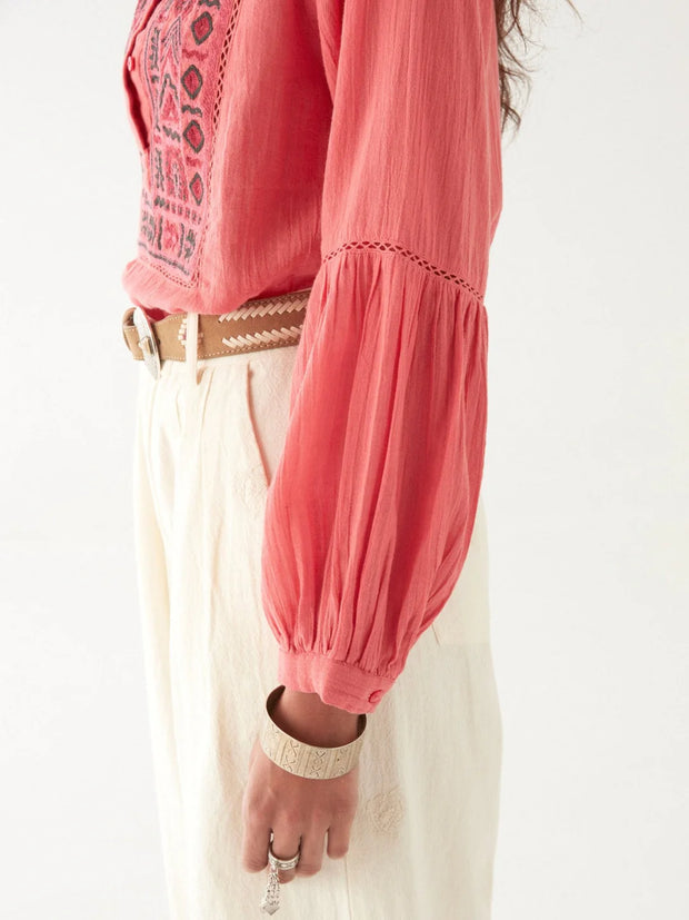 Woman wearing a pink embroidered blouse with a white scarf and beige pants on a white background MAISON HOTEL Shanti Blouse in Strawberry fields Iridescent Sea Fremantle