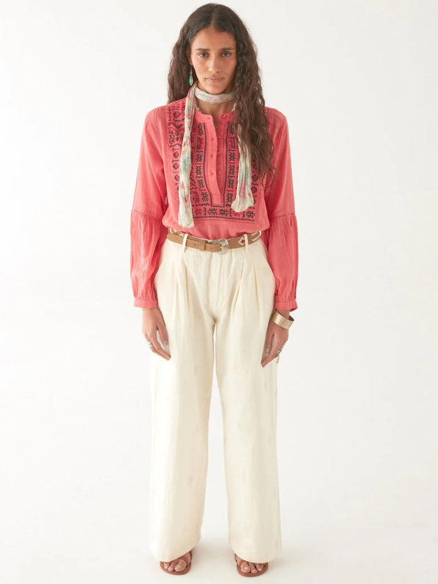 Woman wearing a pink embroidered blouse with a white scarf and beige pants on a white background MAISON HOTEL Shanti Blouse in Strawberry fields Iridescent Sea Fremantle
